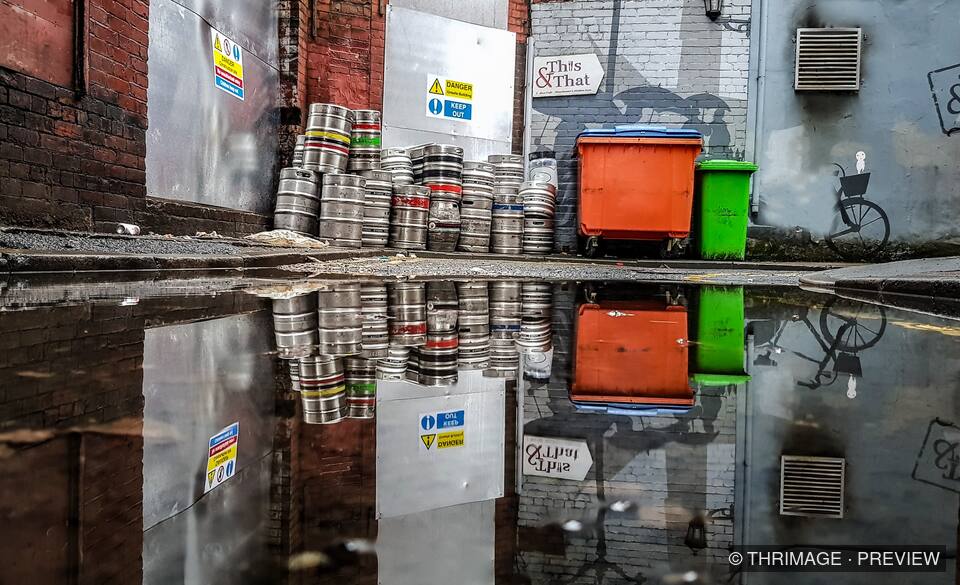 Kegs and wheelie bins reflected in an alley puddle