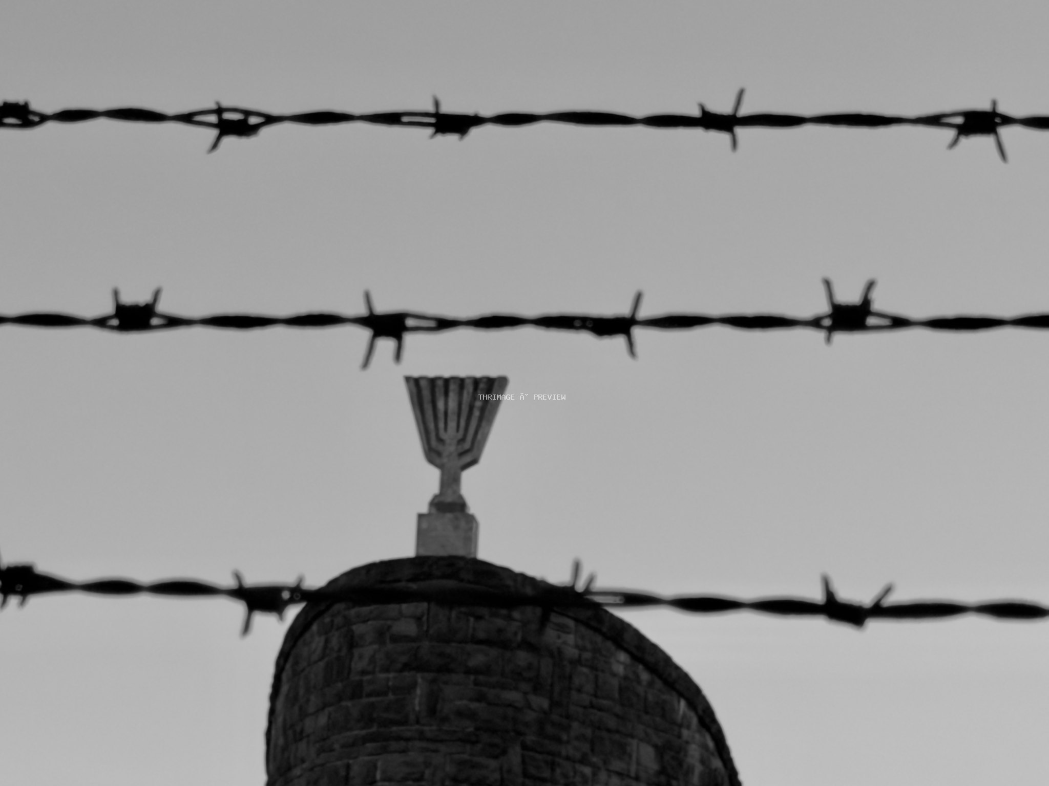 Memorial feature seen through horizontal strands of barbed wire at Dachau Concentration Camp Memorial Site.