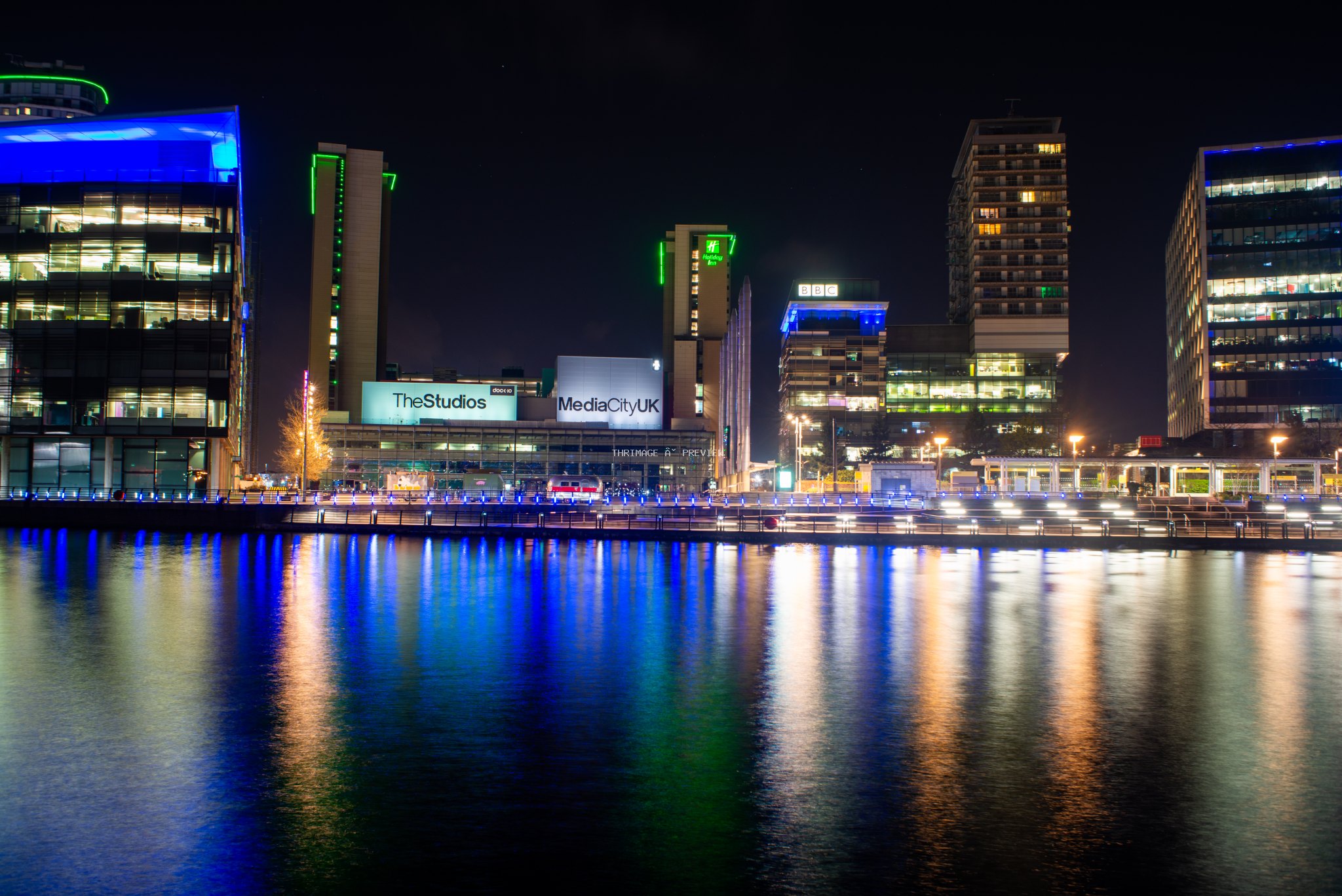 Illuminated MediaCityUK waterfront buildings reflected in dark water at night