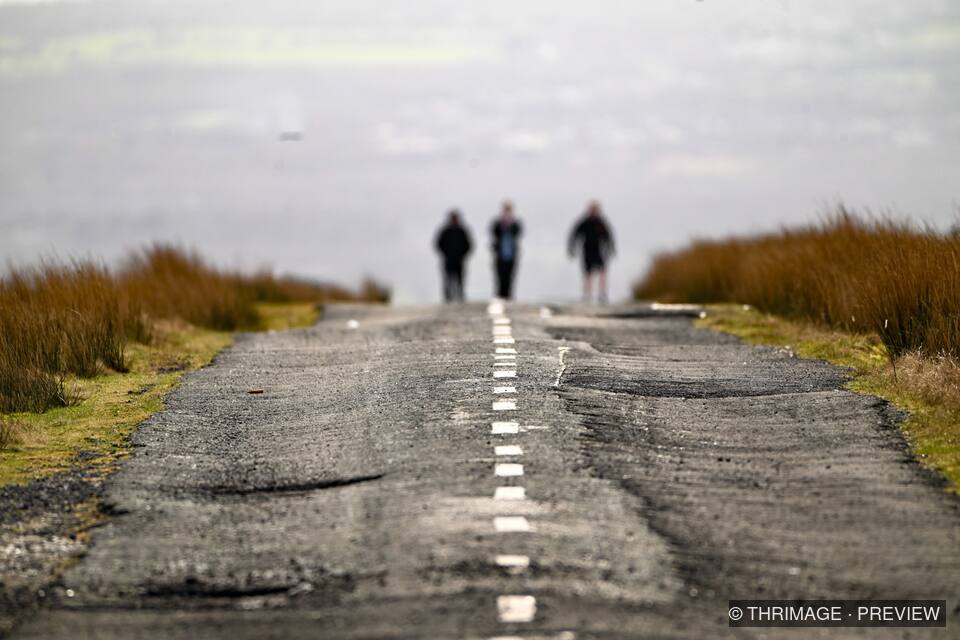 Three distant walkers on a moorland road in hazy light