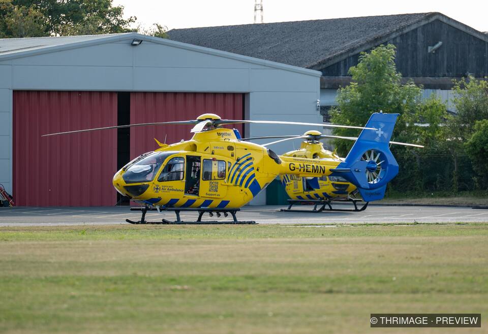 Two North West Air Ambulance helicopters parked outside a hangar