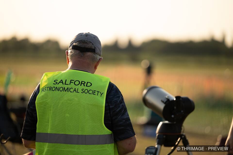 Salford Astronomical Society volunteer beside a telescope at sunset