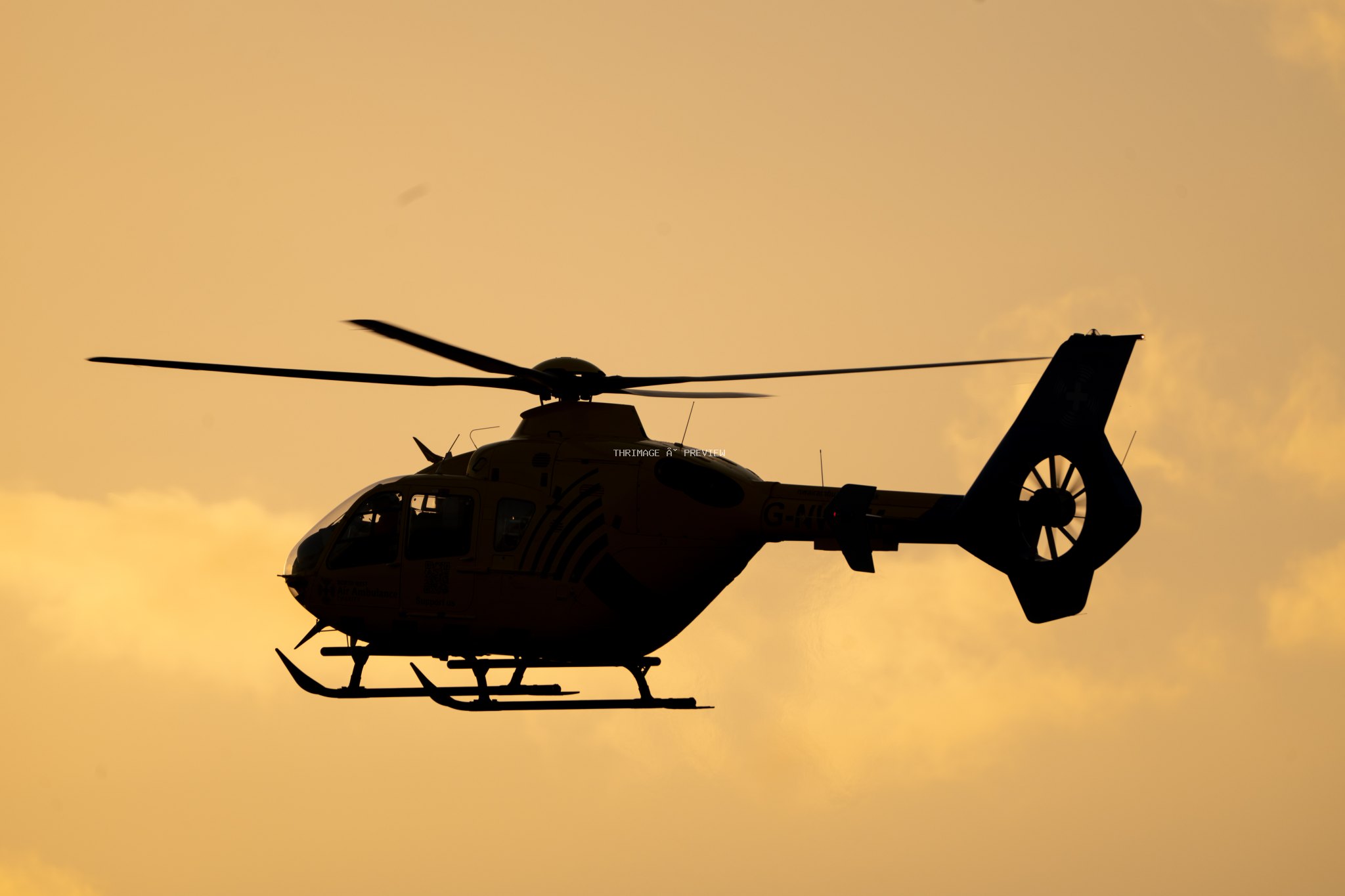 Helicopter in dark silhouette flying against a golden sky