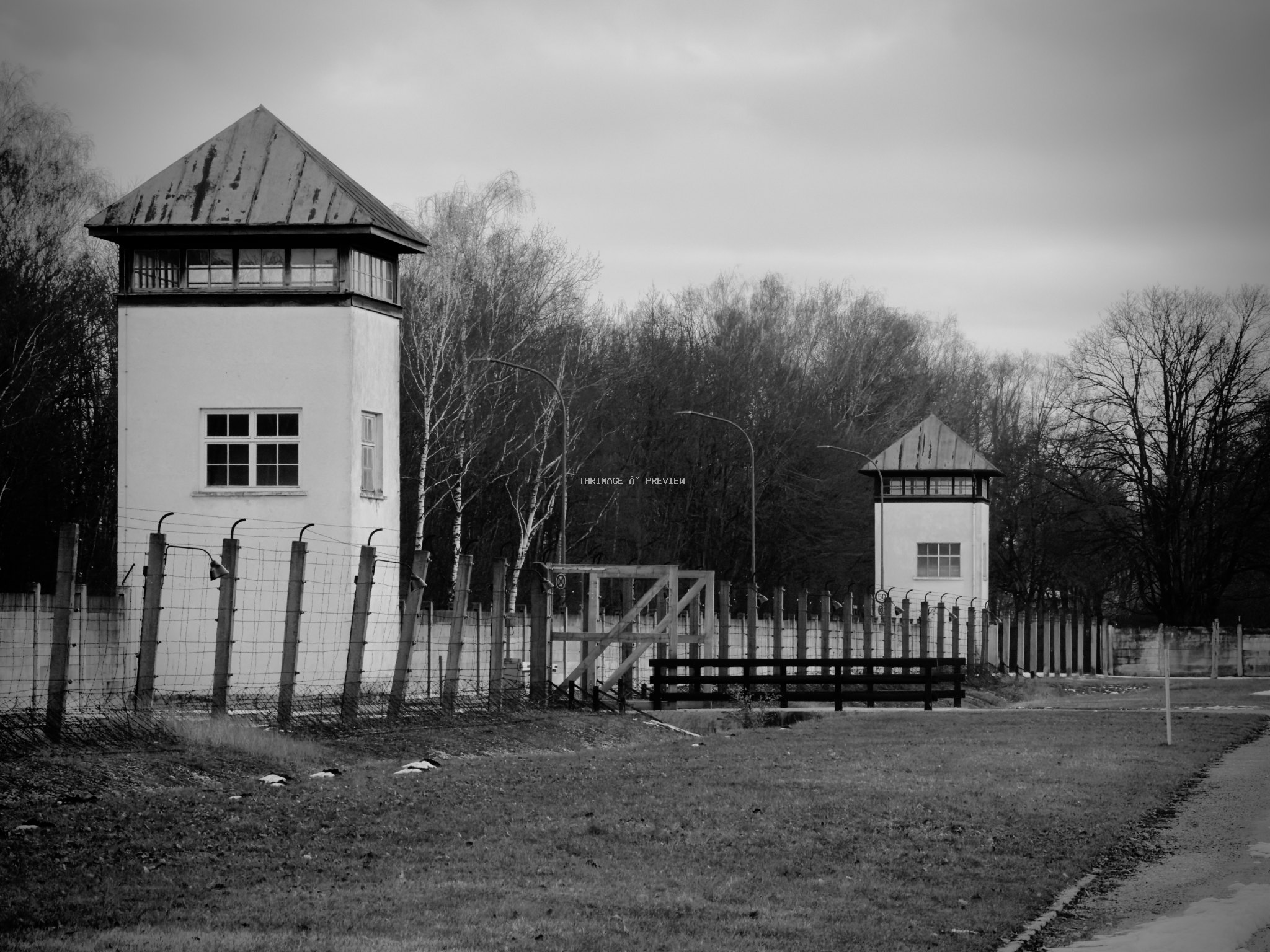 Two guard towers beside the perimeter fence at Dachau Concentration Camp Memorial Site in black and white.